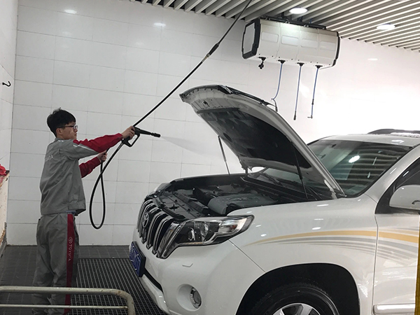 A worker is washing cars with a high pressure cantilever.